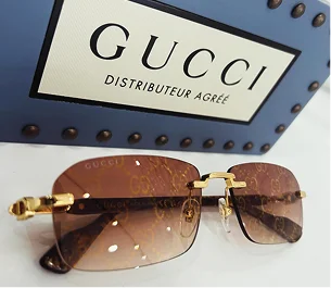 Lunettes de soleil Gucci marron sans monture sur une surface blanche, avec une boîte Gucci bleue en arrière-plan à Montigny-le-Bretonneux dans les Yvelines 78