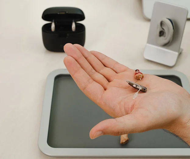 Une main tient des aides auditives discrètes au-dessus d'un plateau, avec un boîtier de chargement à Montigny-le-Bretonneux dans les Yvelines 78
